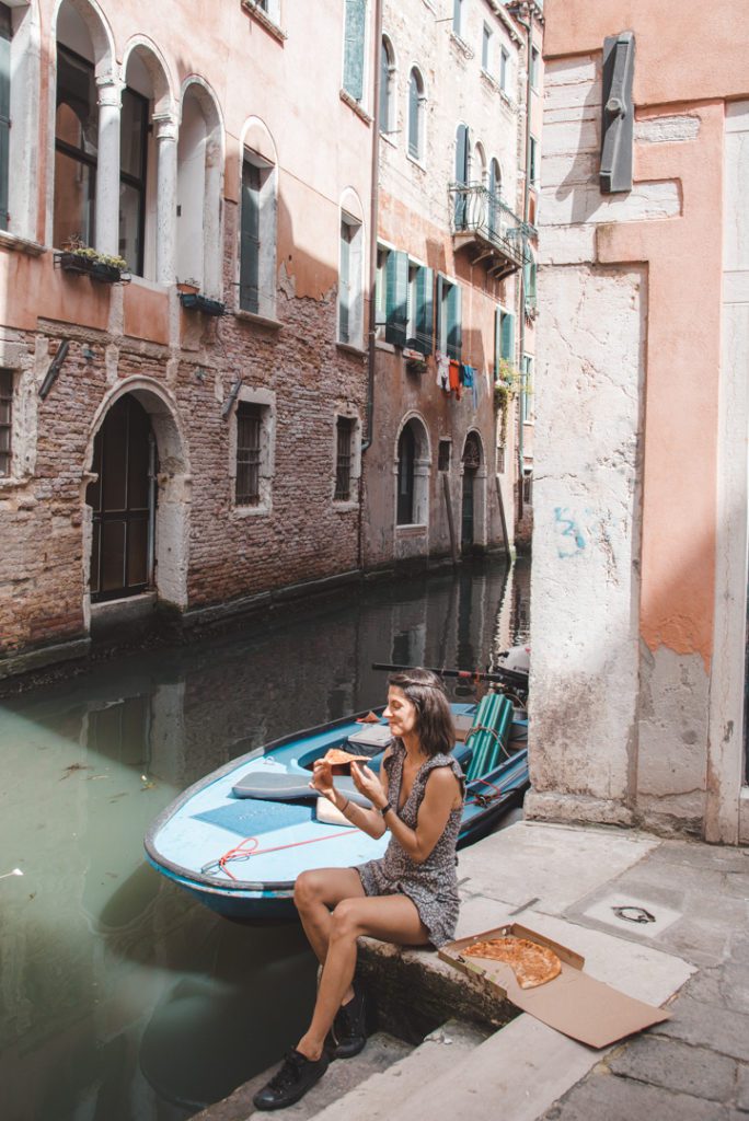 Woman eating pizza by a canal in Venice