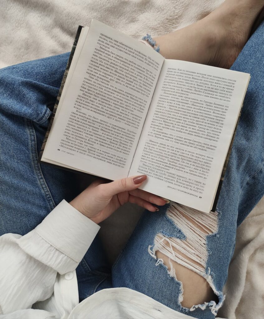 crop faceless woman reading book on bed