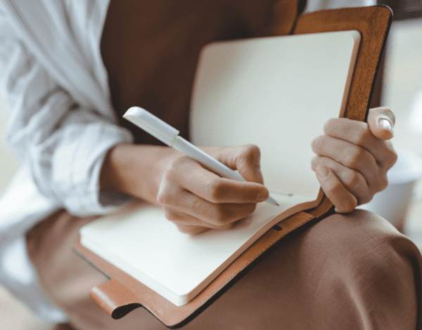 woman journaling in a notebook on her lap- self care journal prompts