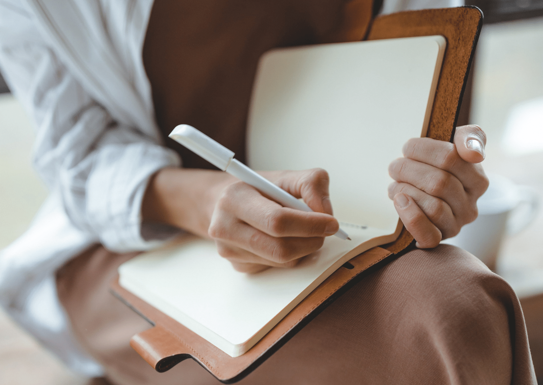 woman journaling in a notebook on her lap- self care journal prompts