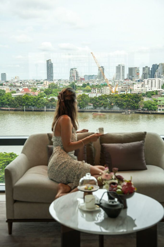 woman looking at the Chao Phraya River from a hotel room in Bangkok