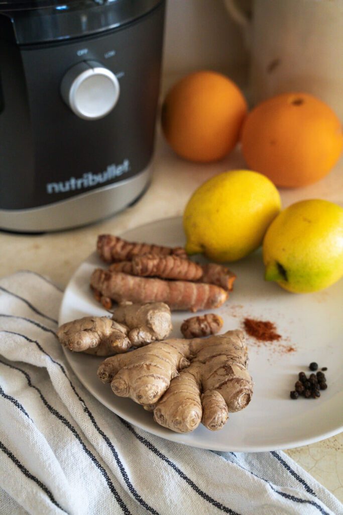 juicer and plate with ingredients for ginger turmeric shot