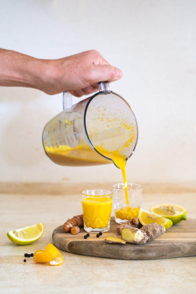 someone pouring turmeric ginger shots into glasses
