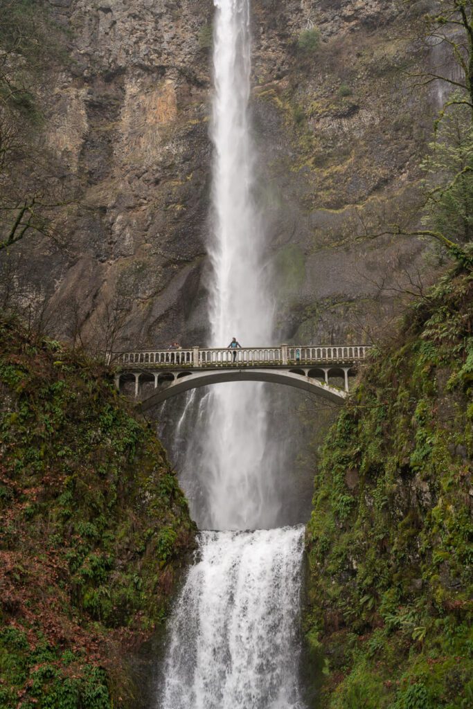 woman on a bridge crossing a dramatic waterfall