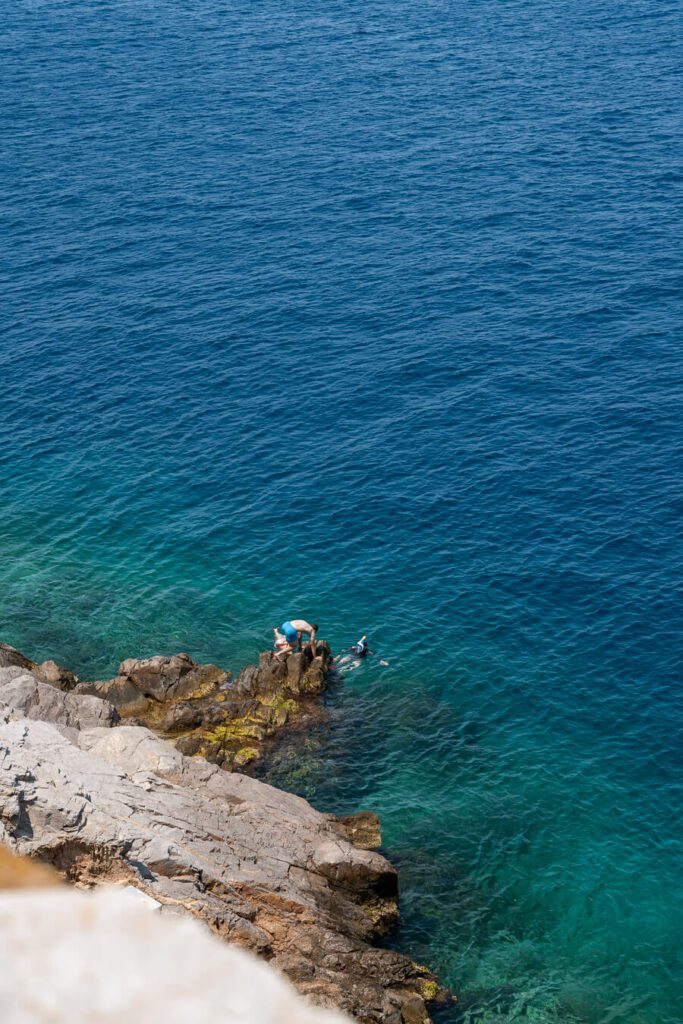 man clambering up rocks on a beach in hydra greece